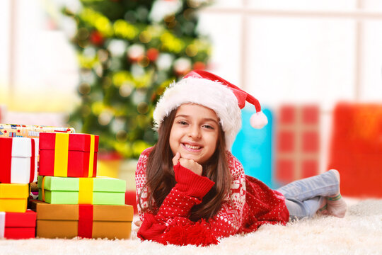 Happy little girl lying on a carpet with Christmas presents looking into the camera and smiling.