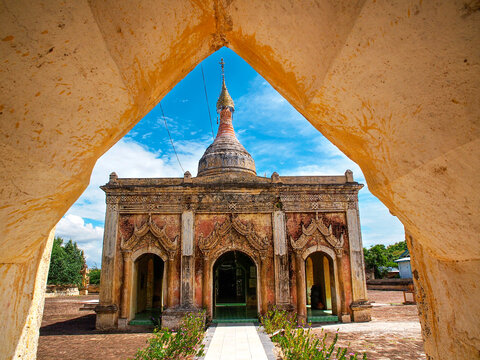 Hsu Taung Pyi Pagoda framed by an old brick arch in the Bagan archaeological zone in Myanmar, ancient Buddhist temple rising above the temple plain under a soft blue sky and evening light