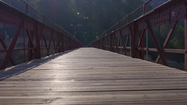 Sunlit wooden footbridge with metal railings above the wooded Huecar gorge in Cuenca Spain