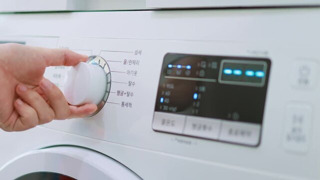 A close-up of a person's hand holding and turning a dial on the control panel of a white washing machine with a digital timer display.