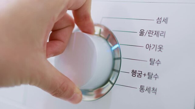A close-up of a person's finger pressing or selecting a setting on a washing machine dial or control panel.