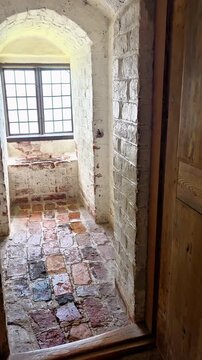 Former toilet room inside Gripsholm Castle in Mariefred, Sweden, with old brick floor, whitewashed brick walls and a historic window overlooking the water outside.