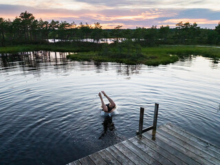 Fototapeta premium Man diving headfirst into bog lake from wooden pier during sunset in Estonian nature reserve outdoor summer swimming active lifestyle travel background