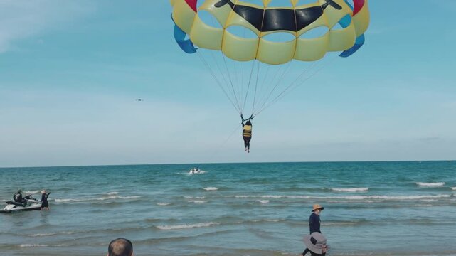 Beachgoers preparing bright yellow and red parasail on sandy beach, people setting up water sport equipment for an adventurous vacation activity, enjoying tropical seaside
