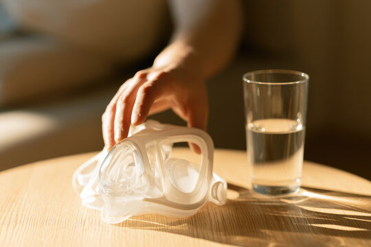 Sleep apnea mask bedside table hand water glass morning sunlight bedroom health care