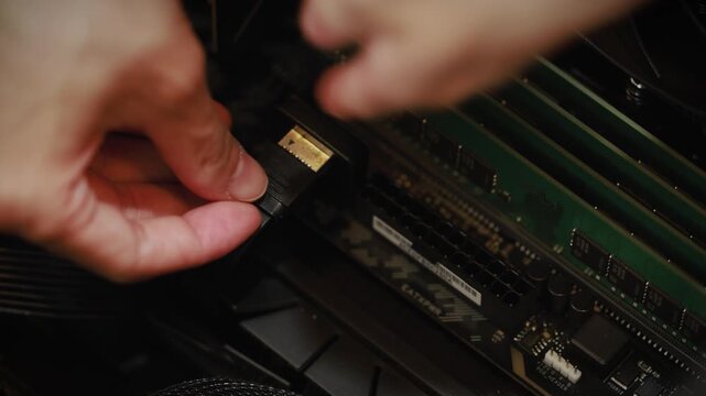 A close-up of a person's hand connecting a gold-plated cable connector to a component inside a desktop computer case.