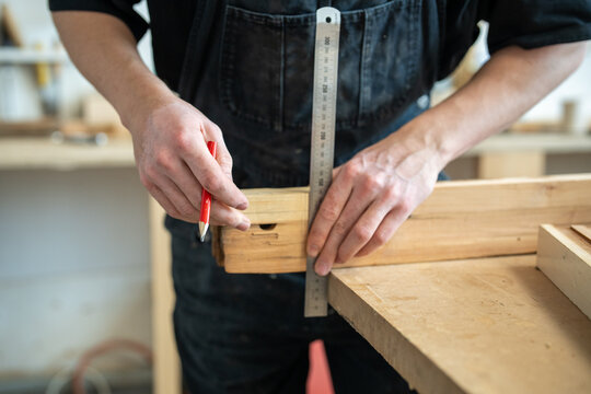 Craftsman working in restoration studio on reconstruction of aged wooden window frame details, master carpenter takes measurements of detail using pencil and ruler, restoration workshop process.