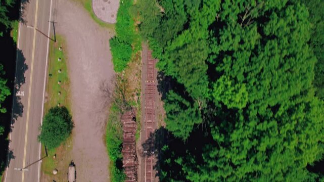 Aerial bird's eye shot of empty train tracks near a traffic intersection, surrounded by green tree tops.