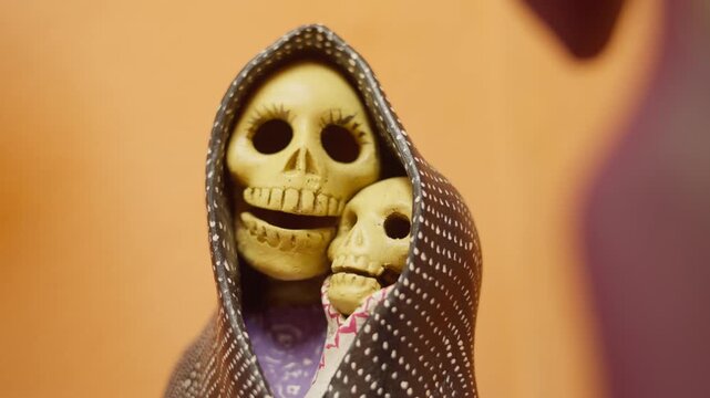 Closeup of handmade Catrina mother holding child in traditional folk art sculpture sharing single garment covering