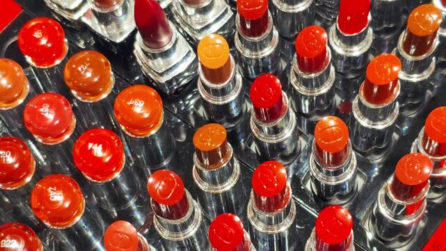 Array of colorful lipsticks displayed in a cosmetics store, showcasing a wide range of red, orange, and brown shades, neatly arranged for selection.