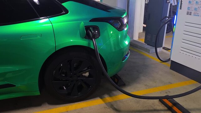 Green electric vehicle charging in underground parking garage, power cable connected to port of car, modern sustainable transportation technology for future of mobility