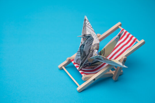 US dollar bill banknote flapping bird rests on beach chair. Financial freedom through passive income, success wealth from investment, interest rate from bank account and so on concept.
