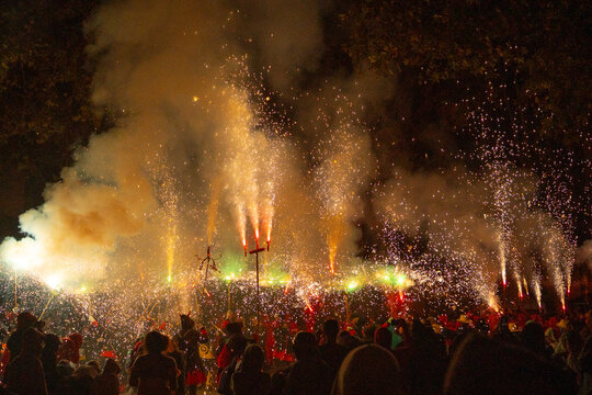 People in devil costumes performance with fireworks sparks on city street night view.

