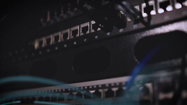 A close-up of ethernet cable ports and network connections on a server rack with blue accent lighting in a dark data center.
