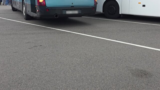 Rear view of turquoise bus and side of white bus parked on asphalt surface of parking lot, with clear white dividing line visible across ground, bus arrival at the station