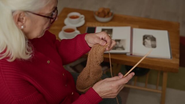 Senior Caucasian woman knitting brown yarn with wooden needles while sitting at home. Footage is ideal for retirement lifestyle commercials, active aging campaigns, or hobby promotions