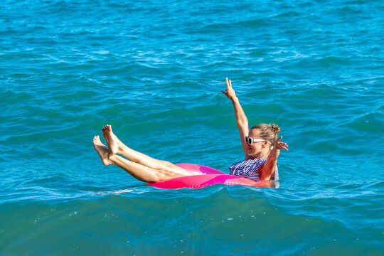 Joyful vacation moment with young blonde woman relaxing on a bright pink inflatable ring in the sea