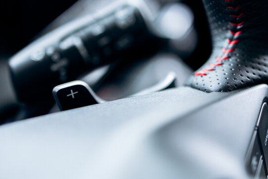 Car interior close up showing performance driving controls with a paddle shifter and red stitching on the steering wheel