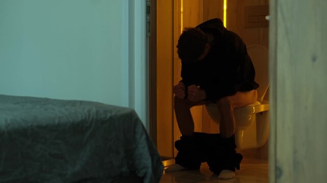 Man struggling with painful bowel movement while sitting on toilet at home, constipation and bathroom discomfort concept