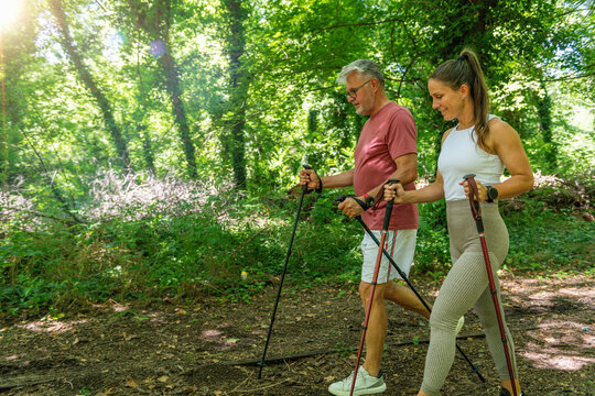 Senior participant performing a guided walking exercise using Nordic poles while receiving professional coaching to enhance cardiovascular fitness, functional movement, and healthy aging.