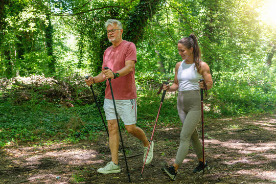 Senior man taking part in a Nordic walking training session with instructor supervision to develop coordination, stamina, walking technique, and full-body fitness in a natural environment.