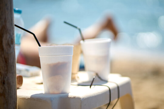 Close-up of two white disposable cups with straws placed on a table near the beach