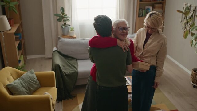 Senior Caucasian woman standing up from armchair to greet young adult Caucasian man and middle aged Caucasian woman bringing gift box. Video is perfect for senior care and family commercials