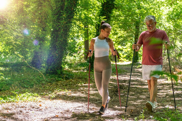 Fototapeta premium Fitness coach leading a senior through a Nordic walking session designed to improve walking mechanics, aerobic capacity, balance, coordination, and long-term physical wellness outdoors.