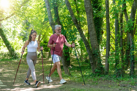 Senior man and fitness trainer enjoying a Nordic walking session in a natural park environment, promoting cardiovascular fitness, functional movement, balance, and long-term active living.