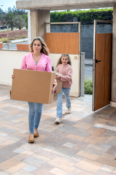 Mother and daughter carrying moving boxes into their new home
