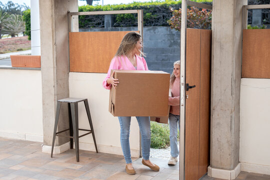 Mother and daughter carrying moving boxes into their new home