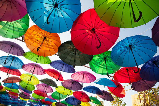 Red, green, blue, and orange umbrellas hang in a colorful outdoor display, vibrant festival decoration, creative background.