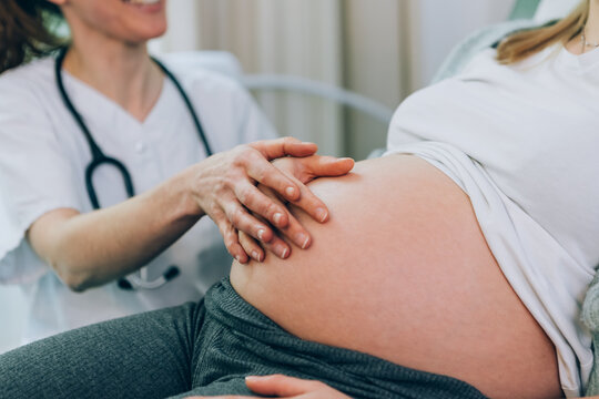 Close-up of a bare baby bump - a midwife rests a reassuring hand over the hand of a pregnant woman during a prenatal visit