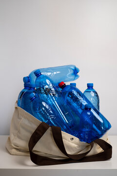 Reusable canvas tote bag overflowing with empty blue plastic bottles for recycling concept	
