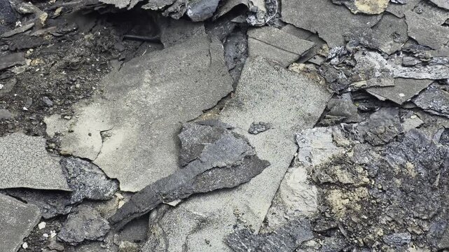 Pile of old roofing felt and bitumen material removed from building roof during repair work, discarded fragments of waterproof layers and asphalt shingles creating a textured background.