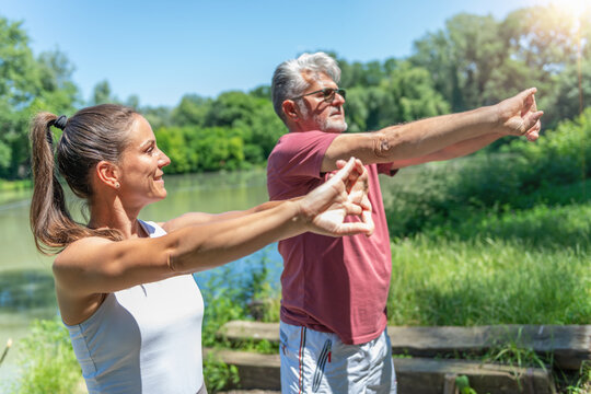 Senior man and fitness coach performing a guided flexibility exercise in a natural outdoor setting to improve joint mobility, posture, upper body movement, and long-term physical health.