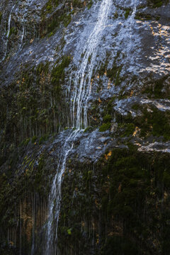 Detail of water streams flowing down a dark mossy rock cliff face in a mountain canyon in the Austrian Alps