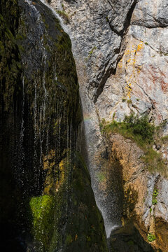 Mountain waterfall cascading down a steep rocky cliff face with green moss in a deep alpine canyon in Austria