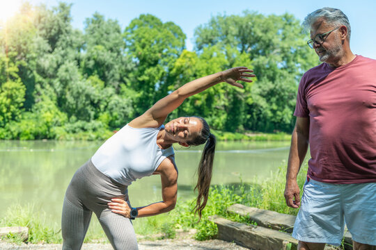 Fitness coach demonstrating a standing side stretch while a senior participant observes proper body alignment, improving flexibility, spinal mobility, posture 