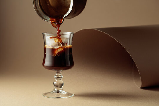Black coffee is poured into a glass with ice.