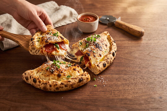 Baked pepperoni calzone pizza slice with melted cheese, marinara sauce, and a hand-lifting slice