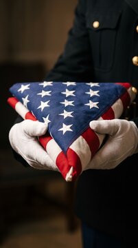 A person in uniform holds a folded American flag with white gloves, symbolizing honor and remembrance. Concept emphasizes patriotism, memorial services, and national pride. Generative AI.