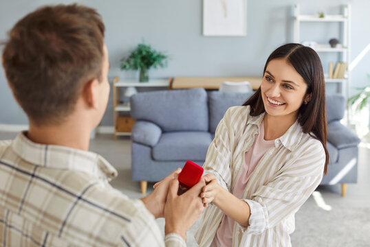 Backside view of a man proposes to a surprised woman at home, giving her a ring as a gift. This romantic moment reflects relationship, love, and the start of journey toward marriage.