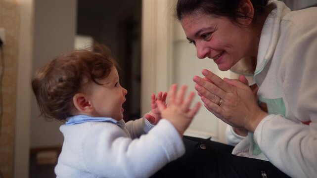 Mother and toddler clap hands together during playful interaction at home, encouraging early learning, joyful communication, secure attachment and positive childhood development