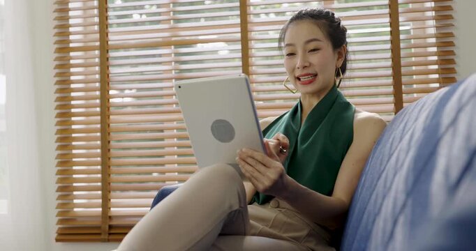 Asian business woman with attractive smile use tablet on coach, Portrait beauty girl relax living room. Technology people connection digital online marketing e-commerce 