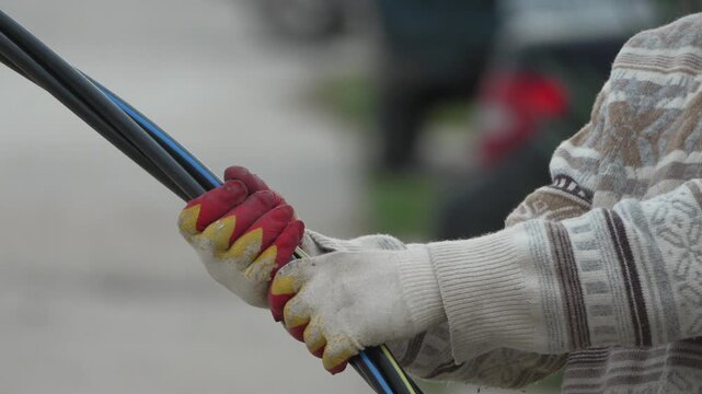 Cable hands worker holding thick black electrical wires while wearing protective industrial gloves during an outdoor installation project