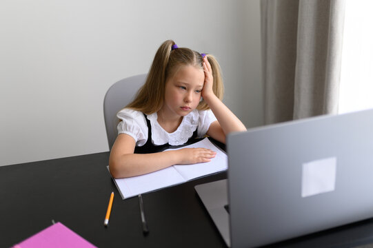 Stressed Schoolgirl Holding Head in Hand looking at Laptop during Online Class