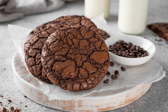 Fresh homemade chocolate brownie cookies on a wooden board with milk on a gray concrete background.