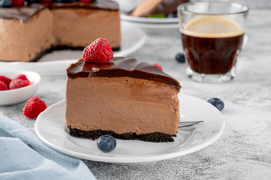 No-bake chocolate cheesecake or mousse cake with chocolate glaze and fresh berries on top on a white plate. Copy space.