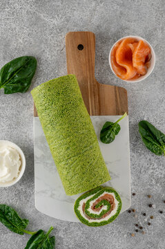 Festive appetizer. Spinach roll with cream cheese and smoked salmon filling on a serving board on a gray background. Top view, copy space.